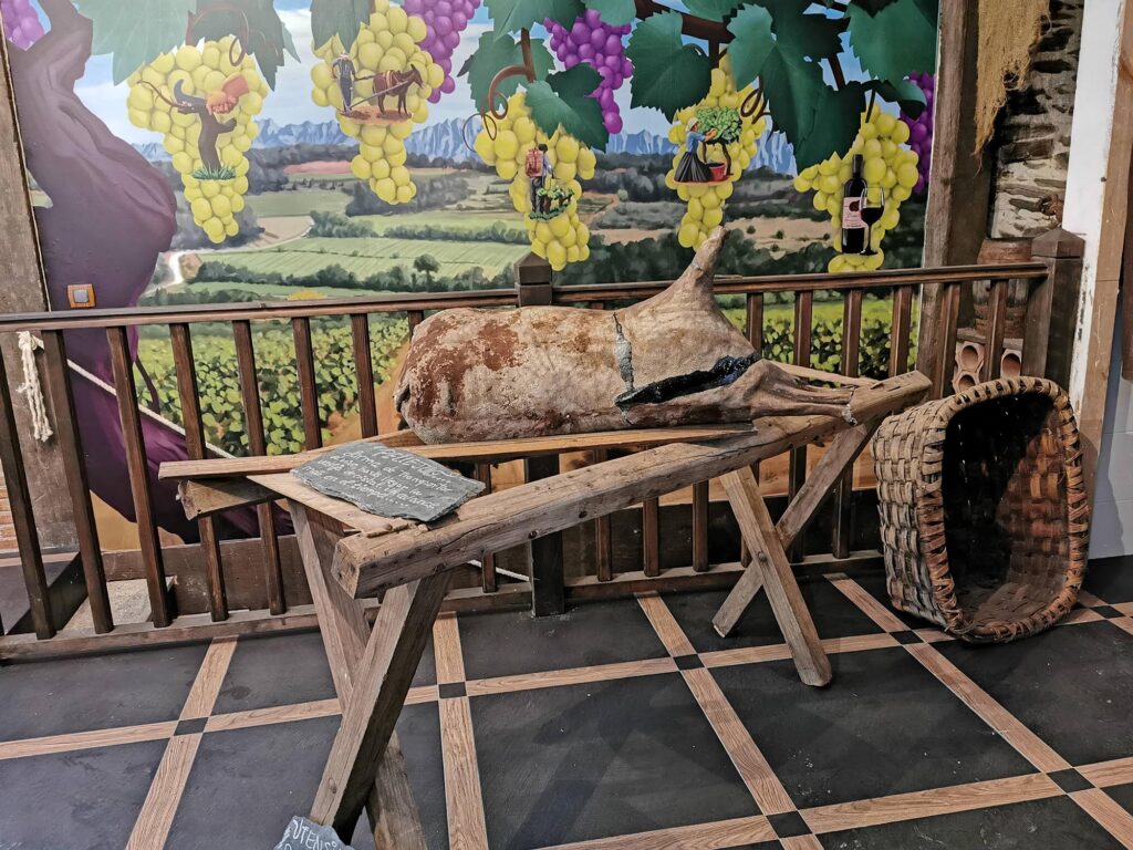 Exposición de aperos agrícolas tradicionales en bodega de la Sierra de Francia con mural de viñedos al fondo