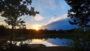 Atardecer en lago tranquilo rodeado de árboles verdes en la Sierra de Francia, cielo azul con nubes doradas