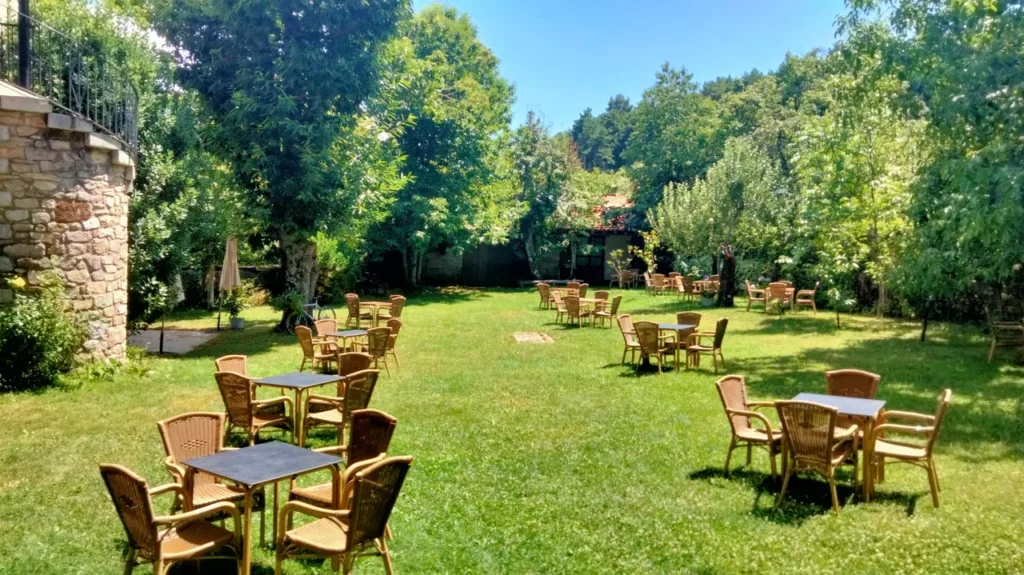Jardín con mesas y sillas de mimbre bajo árboles frondosos en el Hotel Antiguas Eras, Sierra de Francia.