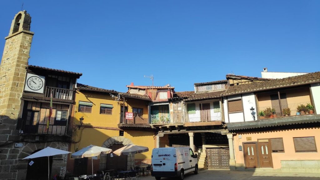 Plaza colonial con iglesia, edificios históricos de colores cálidos y balcones de madera en Sotoserrano, Sierra de Francia.