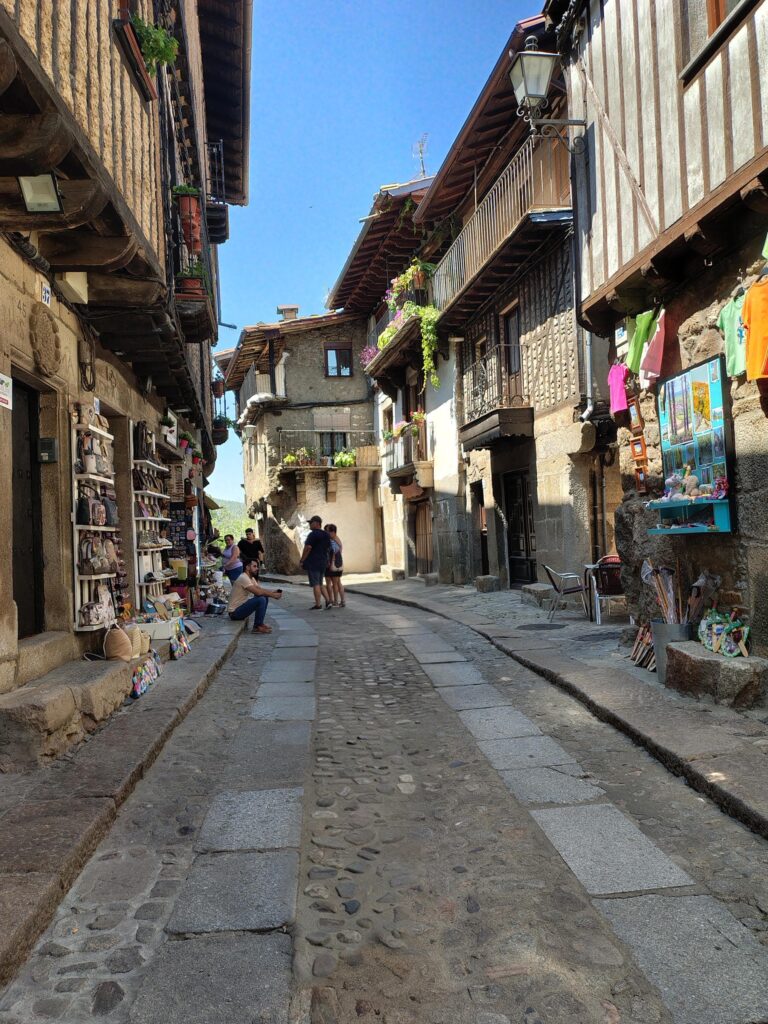 Calle empedrada de La Alberca con casas de piedra, balcones de madera y tiendas de artesanía bajo cielo azul.