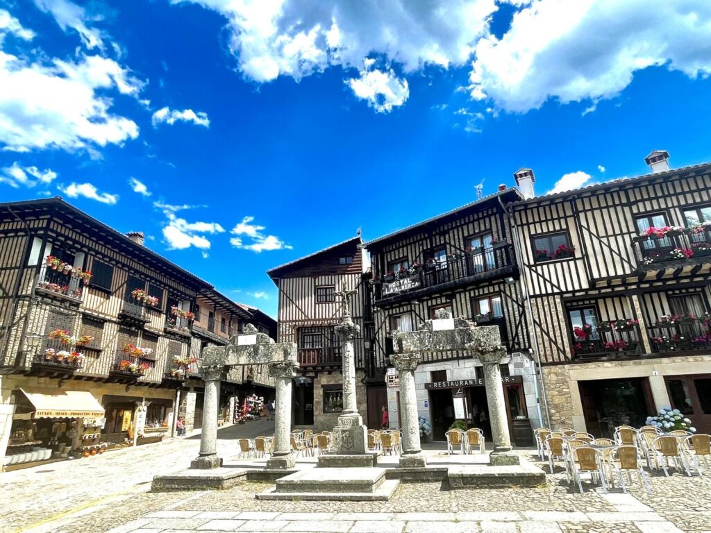Plaza Mayor de La Alberca con arquitectura medieval, casas de entramado de madera, columnas de piedra y cielo azul.