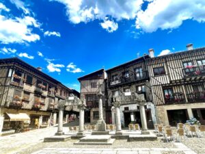 Plaza Mayor de La Alberca con arquitectura medieval, casas de entramado de madera, columnas de piedra y cielo azul.