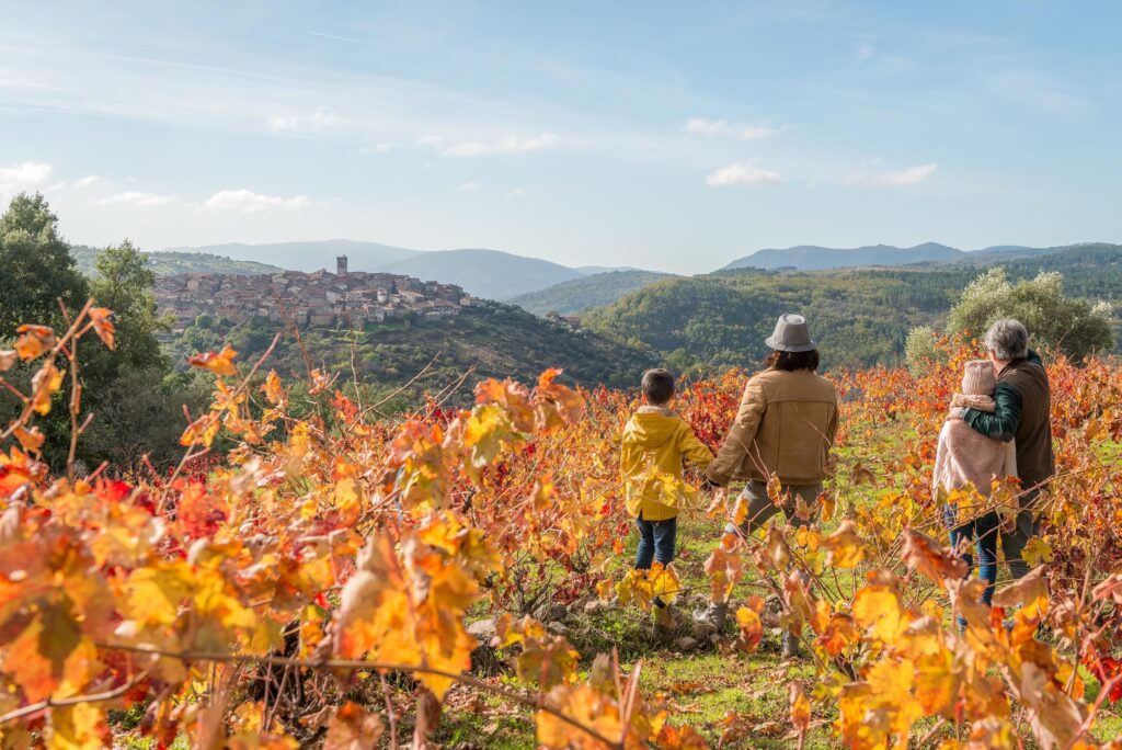 Familia disfrutando otoño entre viñedos coloridos de la Sierra de Francia con pueblo medieval al fondo