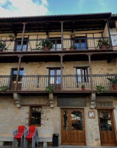 Fachada colonial de restaurante La Botica en Sierra de Francia con balcones de madera, piedra gris y puertas de caoba.