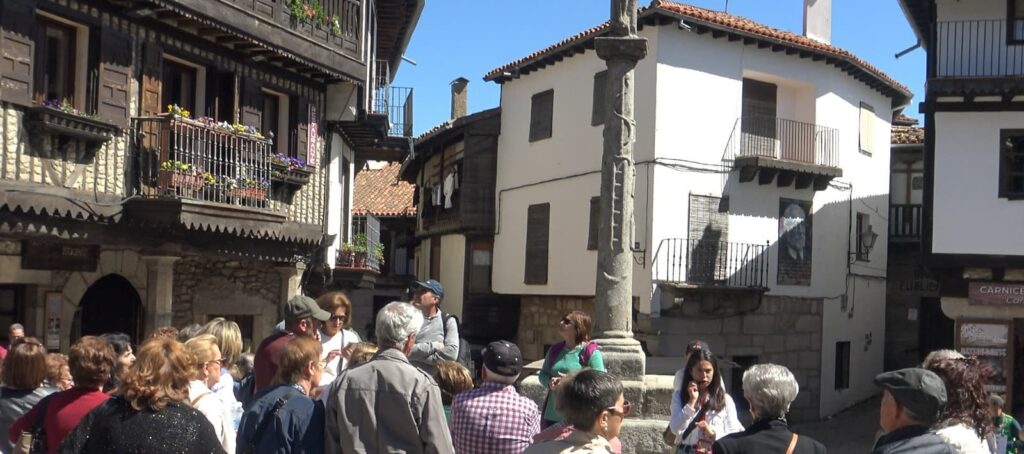 Grupo de turistas en visita guiada por calle histórica de pueblo colonial con arquitectura tradicional de piedra y balcones de hierro.