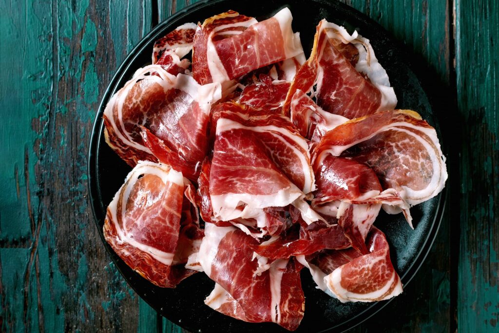 Jamón ibérico de la Sierra de Francia en tabla negra, cortes finos de carne roja con grasa blanca.