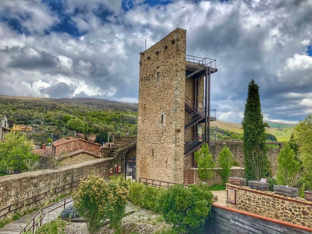 Torre de piedra medieval con escaleras metálicas en Sierra de Francia, rodeada de vegetación y paisaje montañoso.