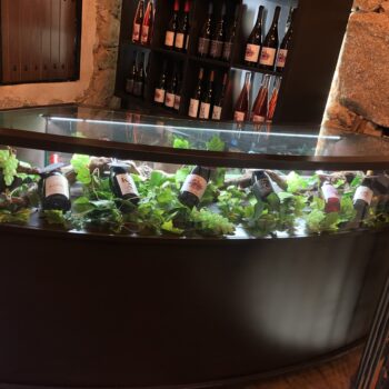 Mostrador de bodega con botellas de vino y decoración de uvas verdes bajo cristal, Sierra de Francia.