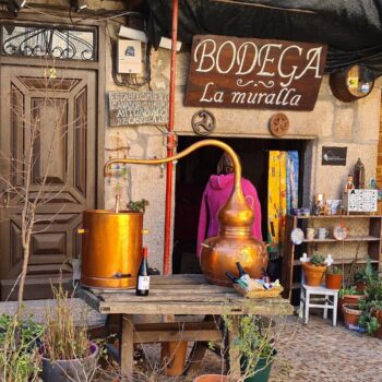 Entrada de la Bodega La Muralla con barril de cobre, decoración artesanal y puerta de madera en la Sierra de Francia.