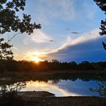 Atardecer en lago tranquilo rodeado de árboles verdes en la Sierra de Francia, cielo azul con nubes doradas