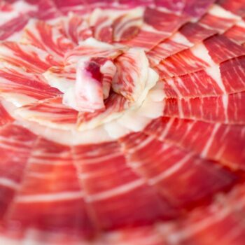 Jamón ibérico cortado en finas lonchas, mostrando su color rojo intenso y veteado de grasa blanca característico.