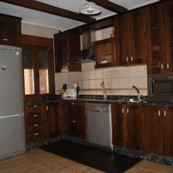 Cocina moderna con muebles de madera oscura, electrodomésticos de acero inoxidable y encimera de granito negro en Casa Rural Arroal.