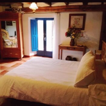 Habitación acogedora de casa rural con cama matrimonial, puertas azules al patio y decoración tradicional de la Sierra de Francia.