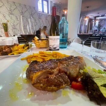 Chuletón jugoso con papas fritas, ensalada fresca y vino tinto en restaurante elegante de la Sierra de Francia.