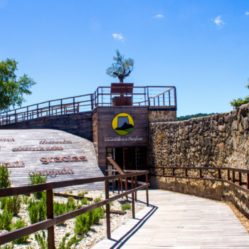 Entrada al Castillo de la Reserva en Sierra de Francia con pasarela de madera, muralla de piedra y señalética.