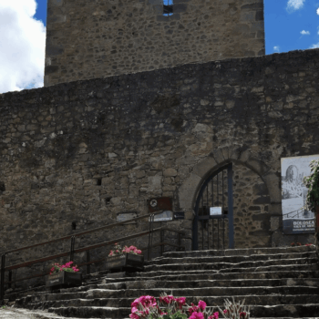Entrada medieval de piedra al Castillo de la Reserva con flores rosas, escaleras y puerta arqueada en la Sierra de Francia.