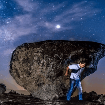 Hombre sostiene enorme roca bajo cielo estrellado en la Sierra de Francia durante la noche.