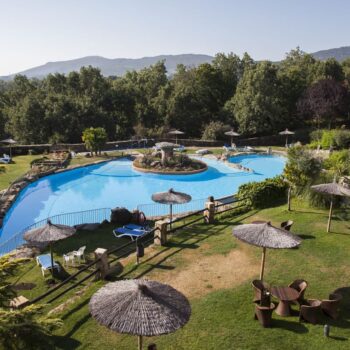 Piscina resort Hotel Doña Teresa en Sierra de Francia con jardines, sombrillas y montañas al fondo.
