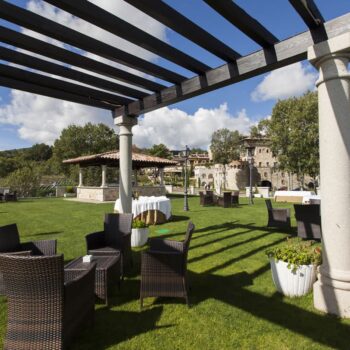 Jardín con pérgola y muebles en Hotel Doña Teresa, Sierra de Francia, con castillo al fondo.