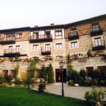 Fachada del Hotel Doña Teresa en la Sierra de Francia, edificio de piedra con balcones de madera, patio ajardinado y flores.