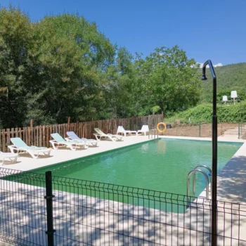 Piscina del Hotel Porta Coeli rodeada de tumbonas blancas, vallado verde y naturaleza de la Sierra de Francia.