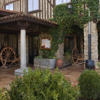 Patio colonial con arcos de piedra, ruedas de madera, vegetación y fachada tradicional de la Sierra de Francia.