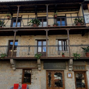Fachada colonial de restaurante La Botica en Sierra de Francia con balcones de madera, piedra gris y puertas de caoba.