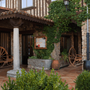 Patio colonial con arcos de piedra, ruedas de madera, enredadera verde y flores en macetas en la Sierra de Francia.