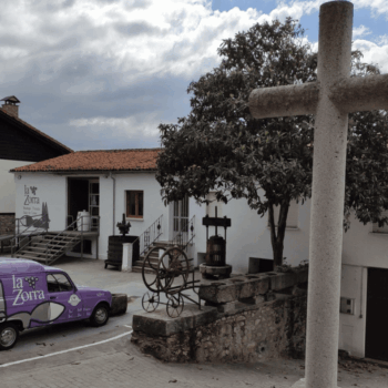 Plaza de la bodega La Zorra con arquitectura tradicional, cruz de piedra y furgoneta púrpura de distribución en la Sierra de Francia.