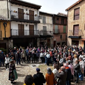 Multitud de turistas en plaza medieval de la Sierra de Francia durante visita guiada, rodeados de arquitectura tradicional de piedra y balcones de hierro forjado.