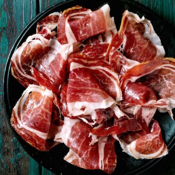 Jamón ibérico de la Sierra de Francia en tabla negra, cortes finos de carne roja con grasa blanca.
